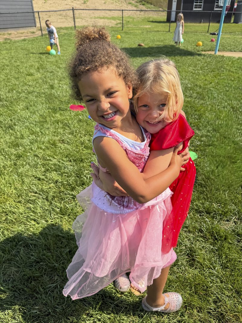 Two children in dress-up clothes hugging on the playground at Theodore's Academy